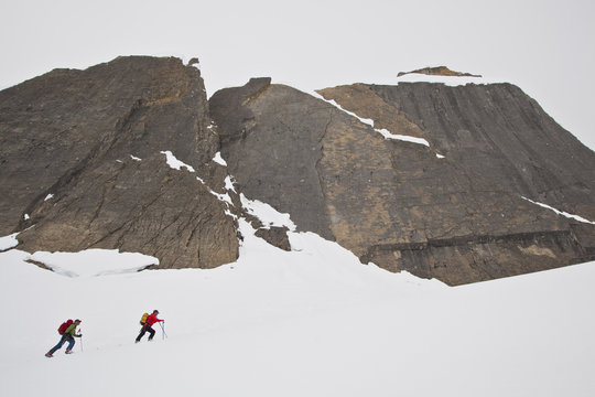 Two male  backcountry skiers skinning up a steep slope onto a glacier, Icefall Lodge, British Columbia, Canada