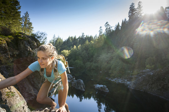 A young woman climbs rocky cliffs at the Sooke Potholes Provincial Park, Vancouver Island, BC, Canada