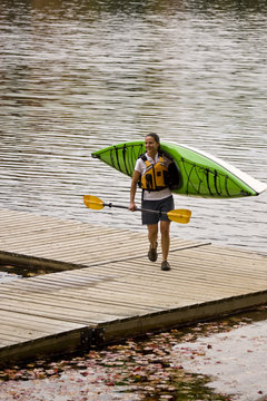 Young woman carrying kayak from water on Oxtongue Lake, Mukoka, Ontario, Canada.
