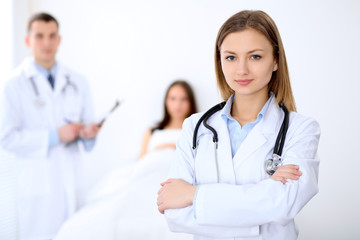 Fototapeta premium Friendly female doctor on the background with patient in the bed and his physician