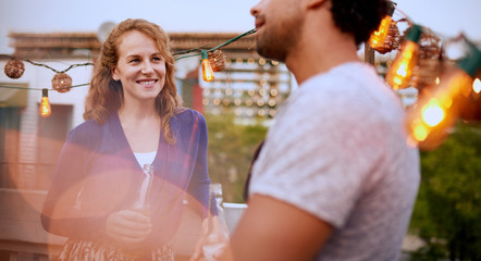 Multi-ethnic millenial couple flirting while having a drink on rooftop patio at sunset