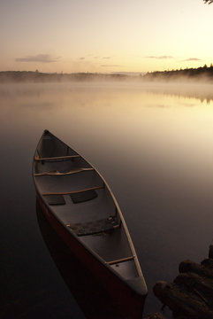 Canoe on shore with predawn scene of a wilderness lake in background in Algonquin park ontario canada
