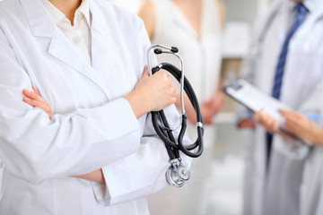 Female doctor holding a stethoscope in his hand, two doctors and patient are on the background