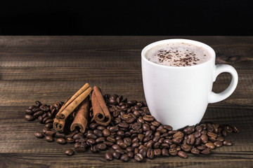 cup of coffee with coffee beans and cinnamon on wooden table. Image with copy space