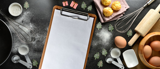 Blank clipboard with kitchen utensils and  christmas toys on black background, copy-space.