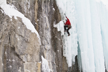 Young man climbs a mix of ice and rock while ice-climbing in Banff National Park near Banff, Alberta, Canada.