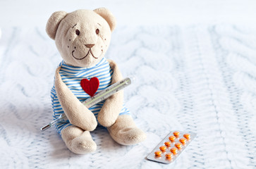 children's soft toy teddy bear with pills takes the temperature of a mercury glass thermometer. child's disease.