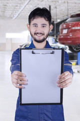 Male mechanic shows clipboard in workshop