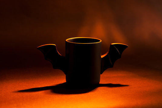 A cup of coffee as a bat for Halloween on black background. Red light and shadow. Toy bat. Halloween concept