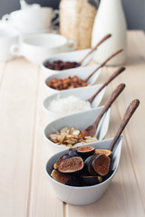 Breakfast bar with healthful choices like nuts, grains, fruit. Fresh figs in focus. Light wood table. 