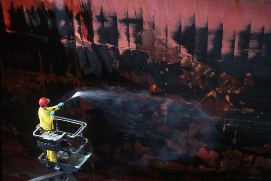 shipyard worker power washes hull of steel ship, Victoria, Vancouver Island, British Columbia, Canada.