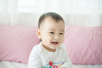 Lovely asian baby girl sitting on bed at her room.