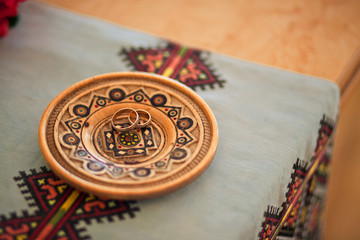 Golden wedding rings lie on the wooden plate with ornament