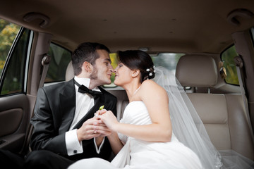 Bride leans to a groom with whiskers for a kiss while they sit i