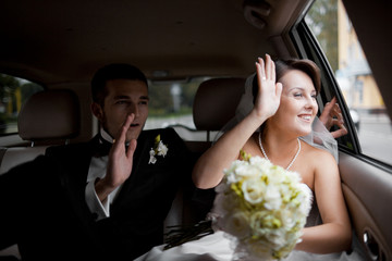 Newlyweds wave with their hands while sitting in the car