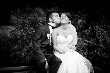 Funny groom leans to bride's cheek while they sit on the back of