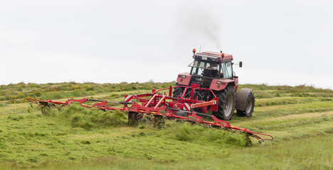 Fototapeta premium Farmer uses tractor to spread hay on the field