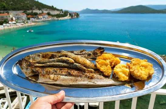 A plate of grilled fish and a beautiful view of the blue sea