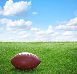American football ball on green grass and blue sky background
