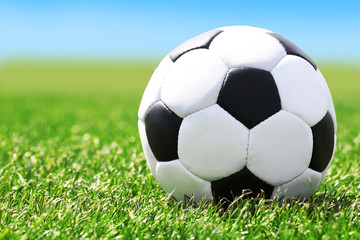 Fototapeta premium Soccer ball on green grass and blue sky background