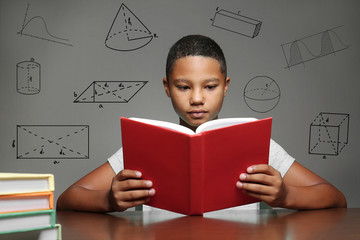 Afro-American boy studying at table. Geometric figures on gray background. Education concept.