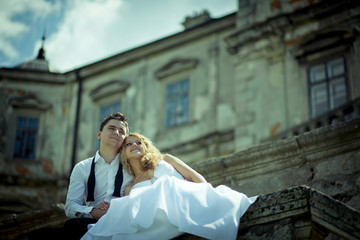 Fototapeta premium Dremy groom hugs his curly bride while they sit on stone handrai