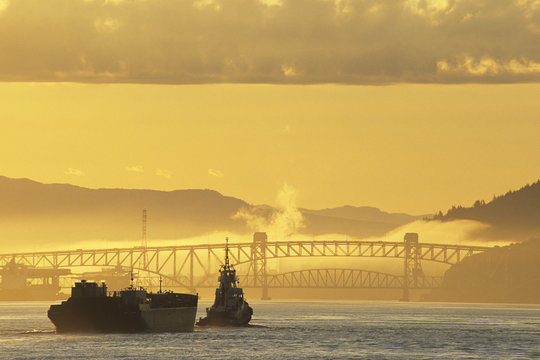 Tugboat with barge approaching the Iron Workers Second Narrows bridge at sunrise, Vancouver, British Columbia, Canada.