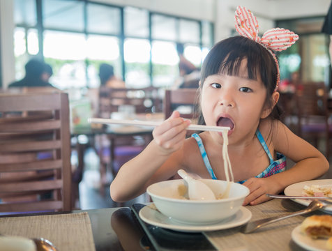 Happy Asian child eating delicious noodle with chopstick, in the