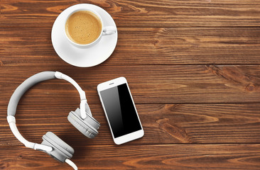 Headphones, mobile phone and cup of coffee on wooden background