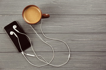 Earphones, mobile phone and cup of coffee on grey wooden background