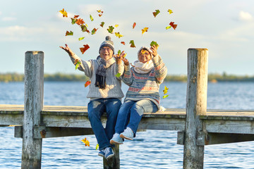 Seniorenpaar wirft buntes Laub in die Luft, Herbsttag am See