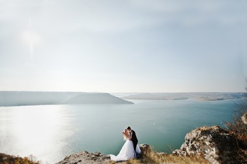 Charming bride in a wreath and elegant groom on landscapes of mountains, water and blue sky at sunny weather