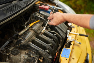 Mechanic changing spark plugs on yellow car outdoor.