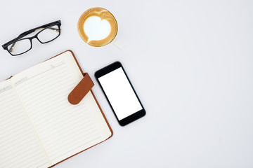 White office desk table with blank screen smartphone, glasses, leather notebook and cup of coffee. Top view with copy space.Office desk table concept.