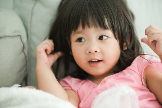 child and happiness concept - smiling little asian girl on sofa at home