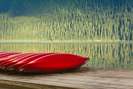 Row of red canoes on jetty by lake, Canada