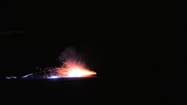 A shower of sparks shoot out sideways on the ground and sparks igniting. HD 1080.
