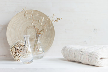 Soft home decor of  glass vase with spikelets and knitted fabric on white wood background. Interior.
