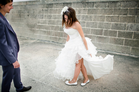 Pretty bride in white ballerina flats stands behind the wall