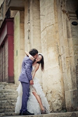 Fototapeta na wymiar Groom in violet suit kisses bride's cheek while she poses in sed