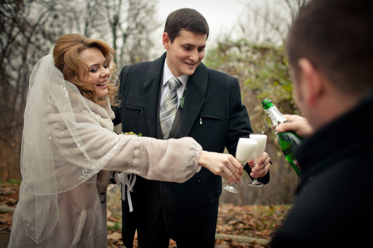 Cheerful newlyweds holds their glasses while man pours champagne