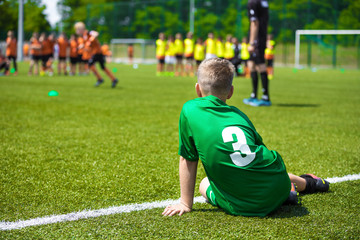 Young caucasian soccer player sitting on grass. Youth football background