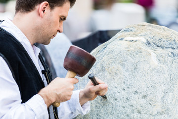 Bildhauer mit Meißel und Klüpfel beim Bearbeiten von Naturstein-Block