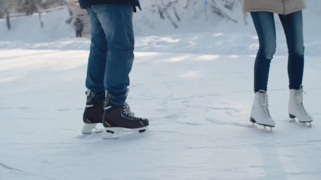 Handheld tracking of young woman ice skating with her boyfriend in ice rink in park, then falling in his arms and laughing