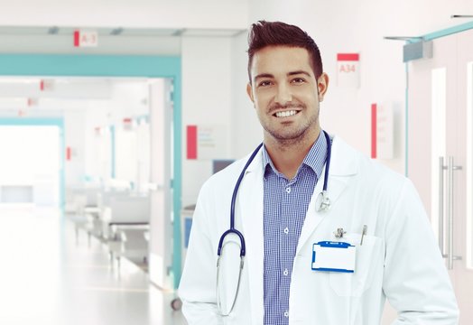Happy young physician standing at hospital hallway