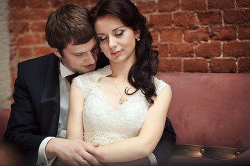 Smiling groom leans to bride's shoulder while she daydreams in h