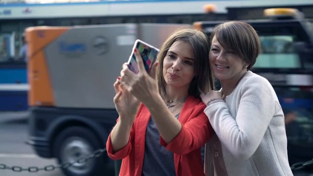 Two pretty girlfriends taking selfie photo with cellphone in city 
