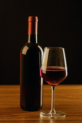 Red wine bottle with glass on black background