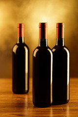 Three red wine bottles with glass on gold background

