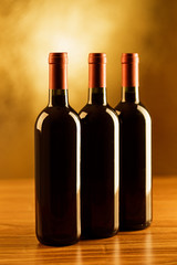 Three bottles of red wine on wooden table and golden background